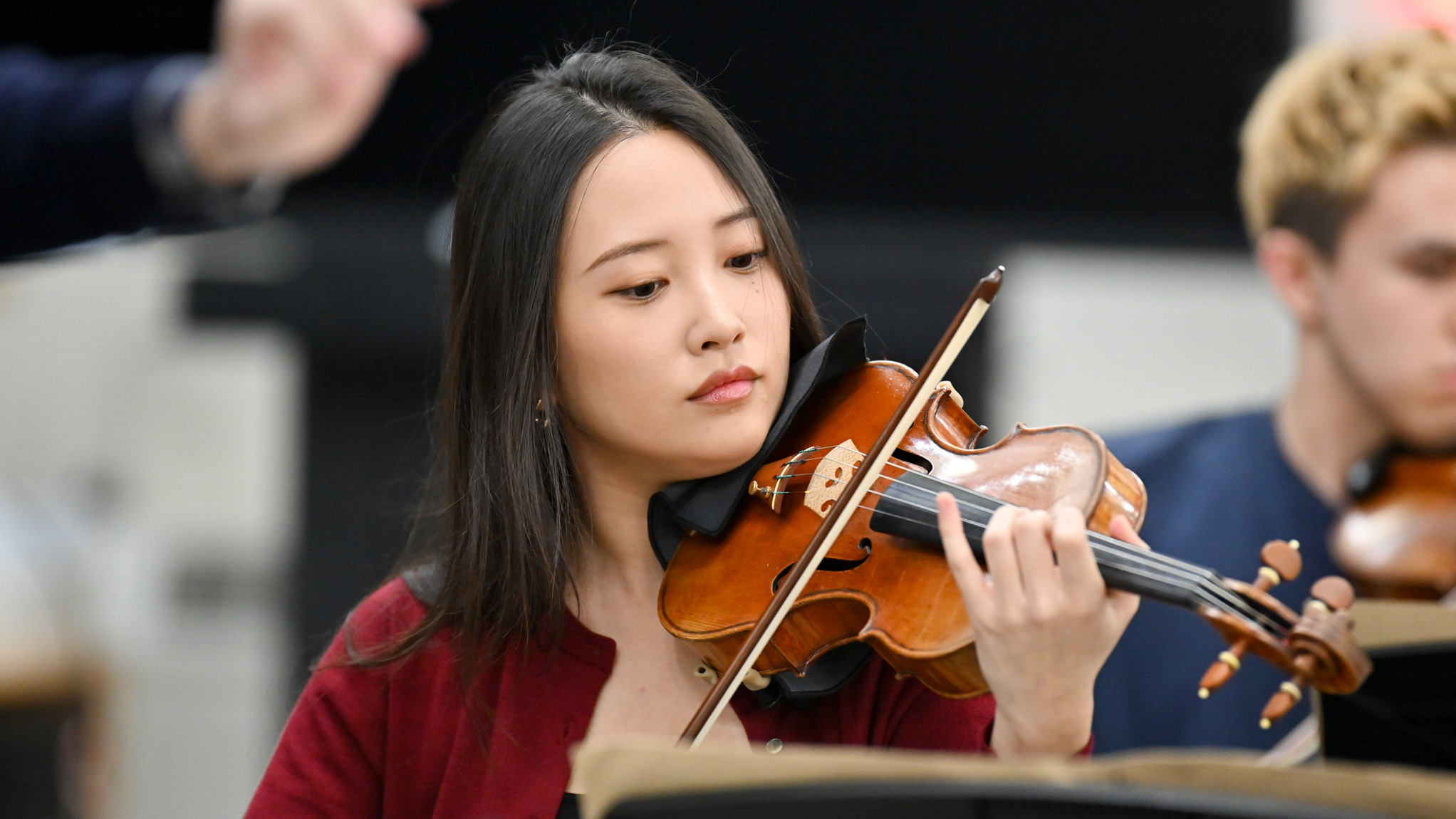 A female student playing the violin in an orchestra rehearsal, in flow.